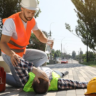 Construction workers, one laying down overcome by heat, other trying to help