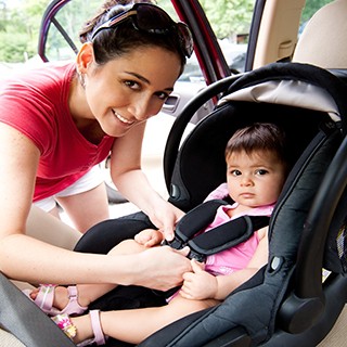 ethnic mother strapping child into car seat