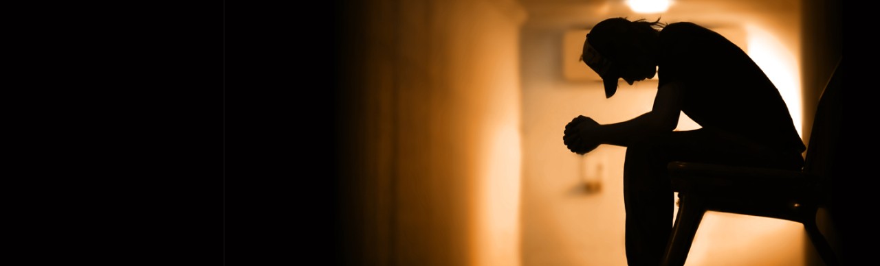 Silouette of young man with ball cap on, looking depressed